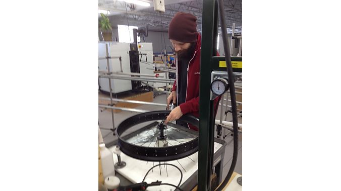 A master wheelbuilder uses a pneumatic tool to place nipples in a fat-bike rim too wide to be accommodated by a Holland wheel-building machine.